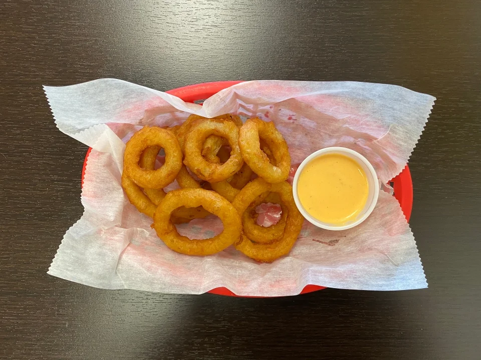 A basket of crispy onion rings served with a small cup of dipping sauce.