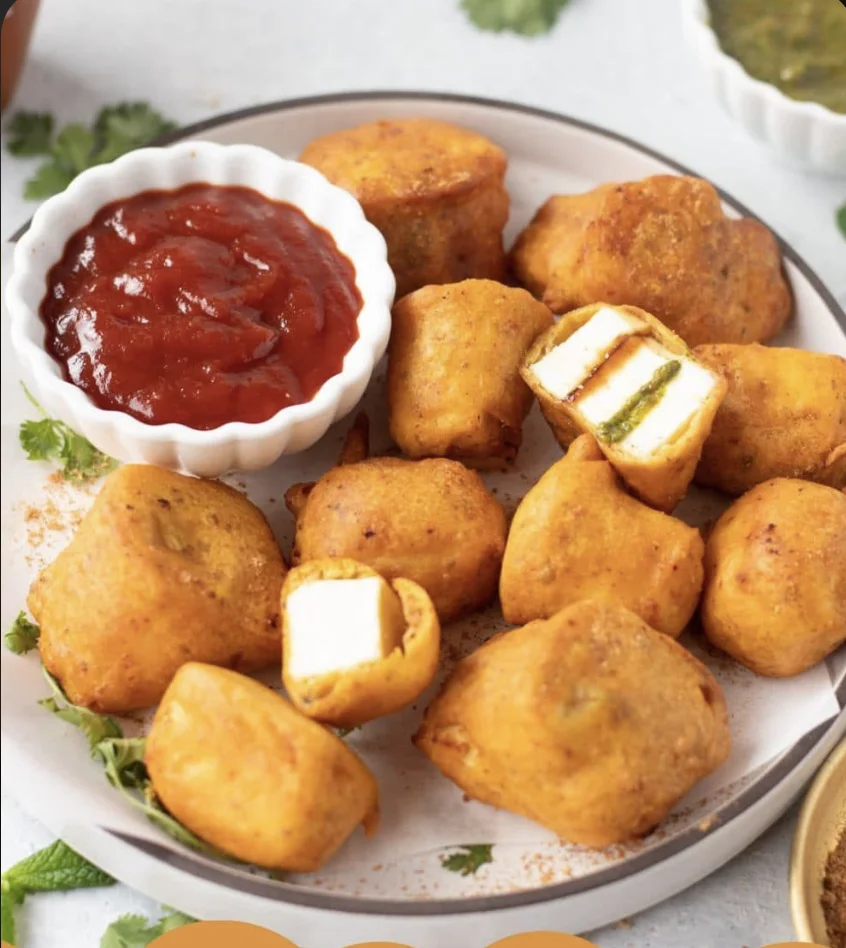 A plate of golden-brown fried snacks with a bowl of tangy red sauce, showcasing a mix of crispy textures and stuffed ingredients.