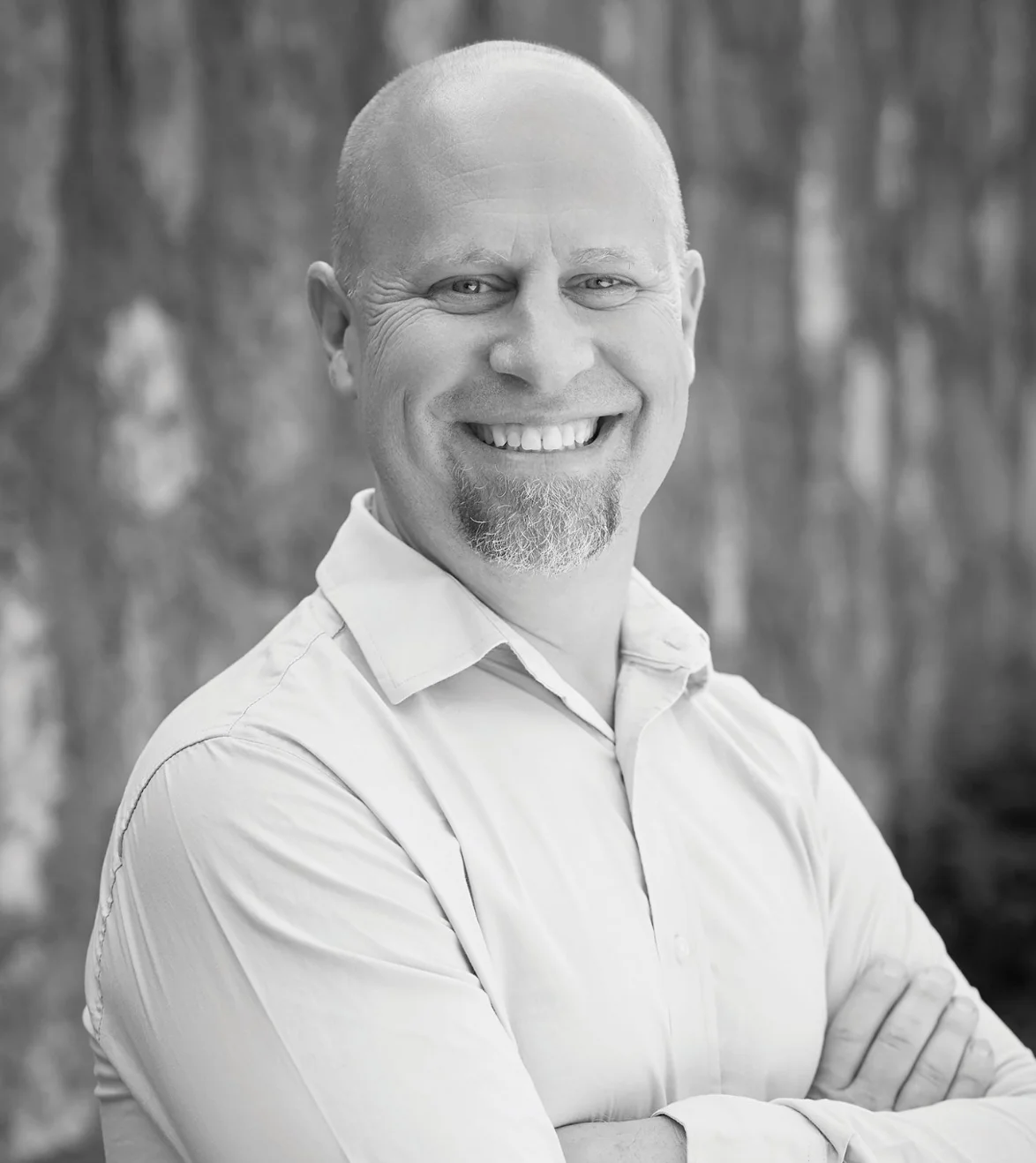 Smiling man in a light shirt with arms crossed against a textured background.