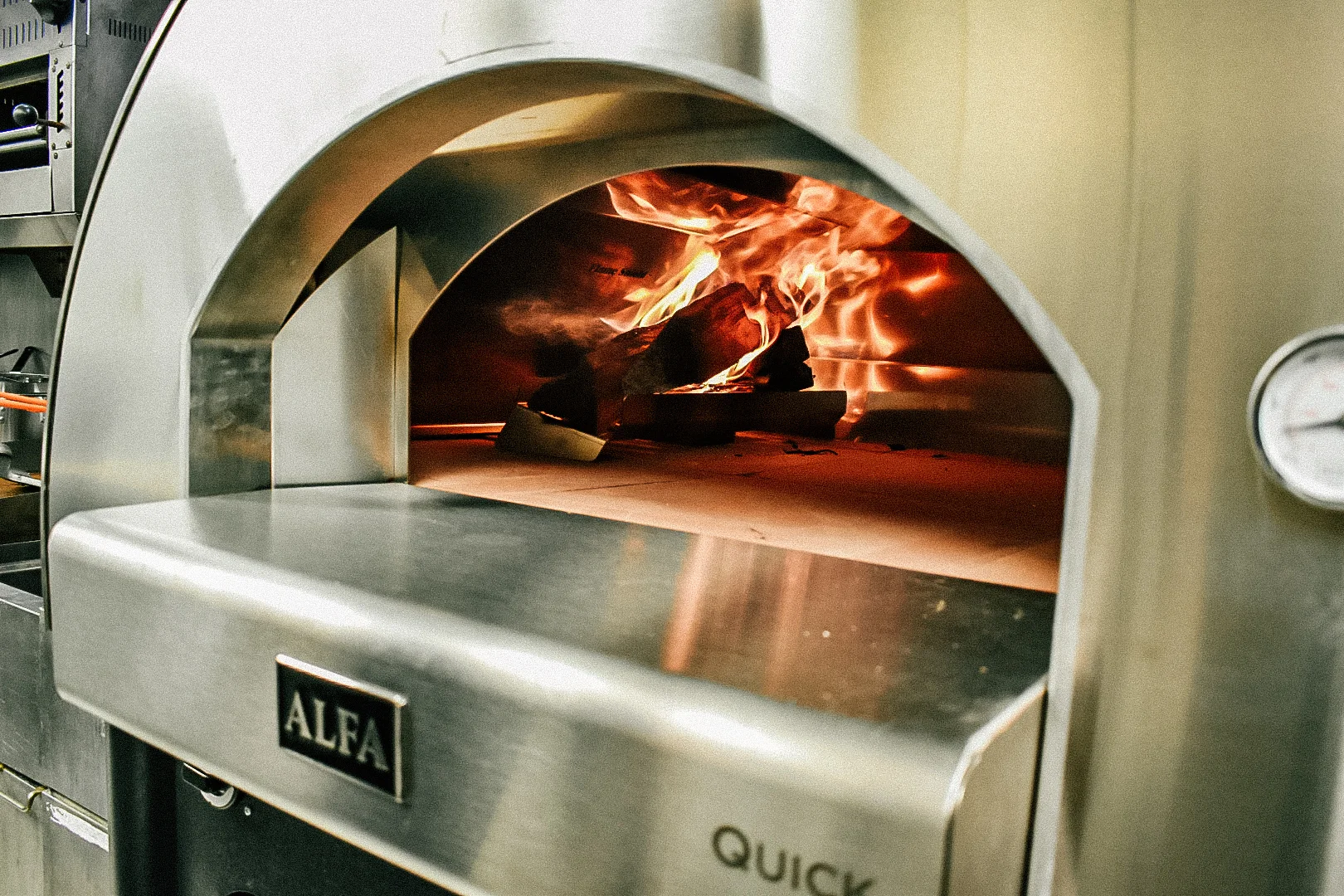 The interior of a pizza oven with flames and wood burning inside, showcasing a stainless steel design.