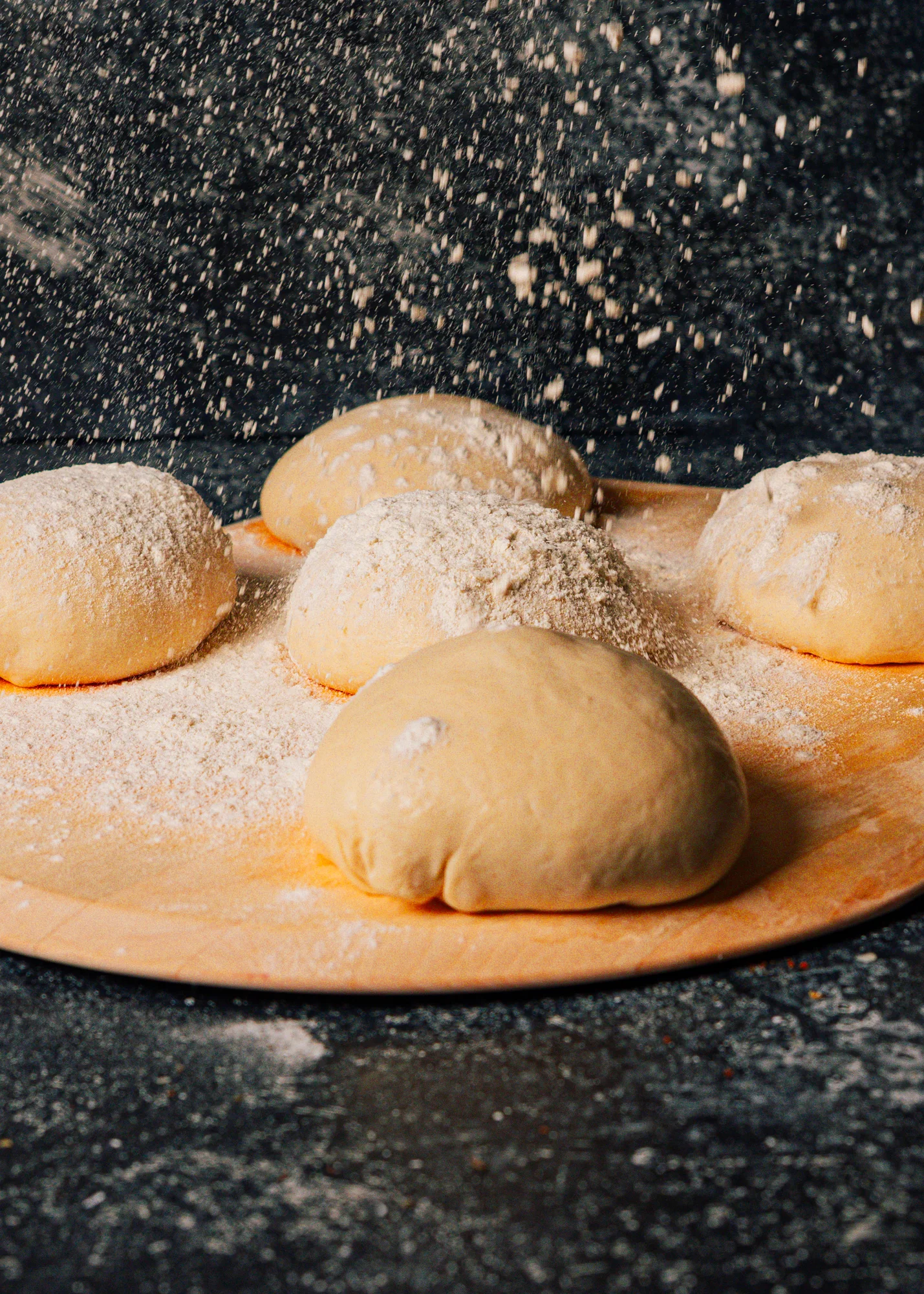 Freshly kneaded pizza dough balls dusted with flour on a wooden board