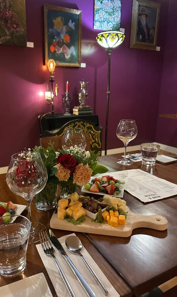 A beautifully set dining table in an inviting restaurant, featuring a floral centerpiece, glassware, and an assortment of fruits arranged on a wooden board.