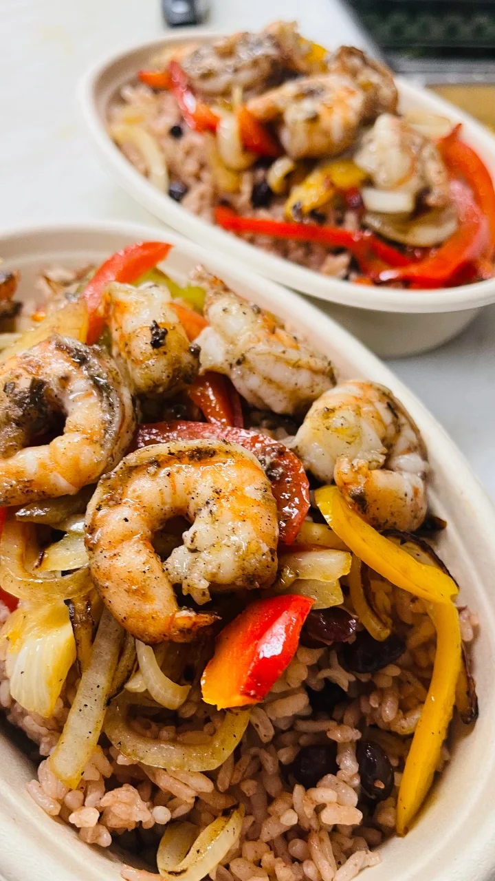 A colorful bowl of shrimp and vegetables served over seasoned rice, featuring bell peppers and onions.