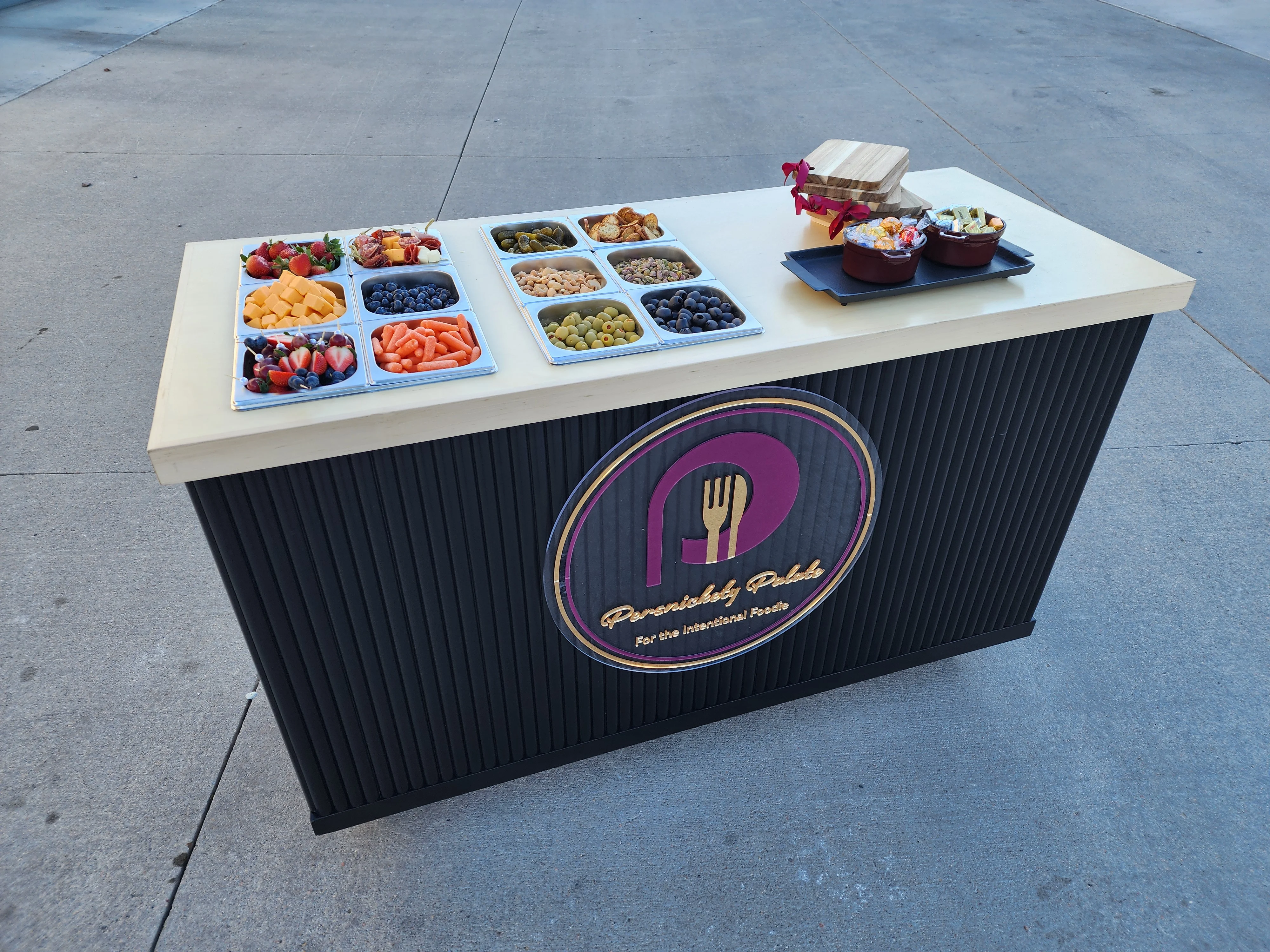 A food cart displaying a variety of fruits, vegetables, and snacks in compartments, with a decorative bow on top.