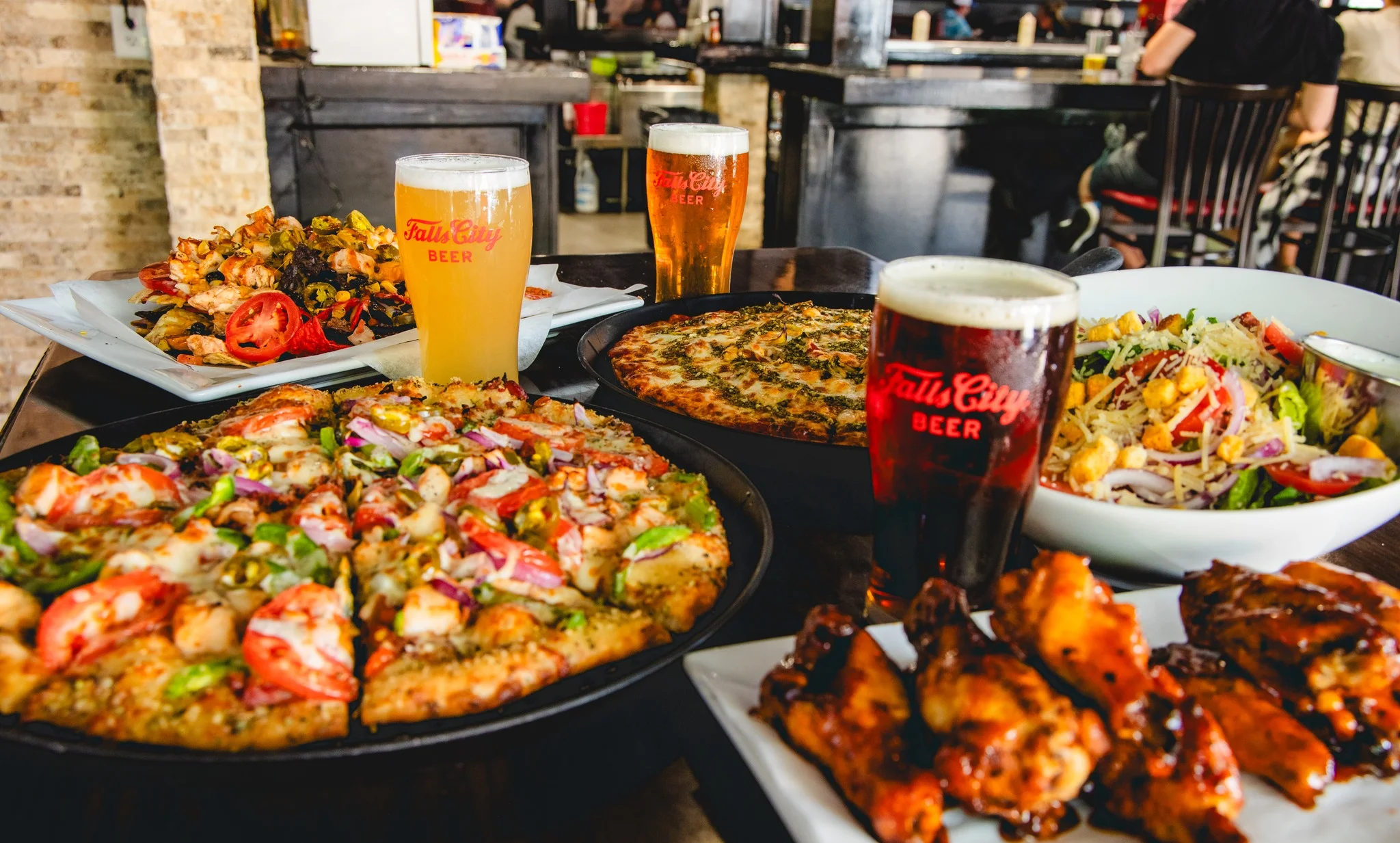 Assorted pizzas and wings with craft beers in a lively restaurant setting