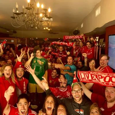 A lively gathering of fans celebrating a sports event, wearing red clothing and holding scarves with team colors in a festive environment.