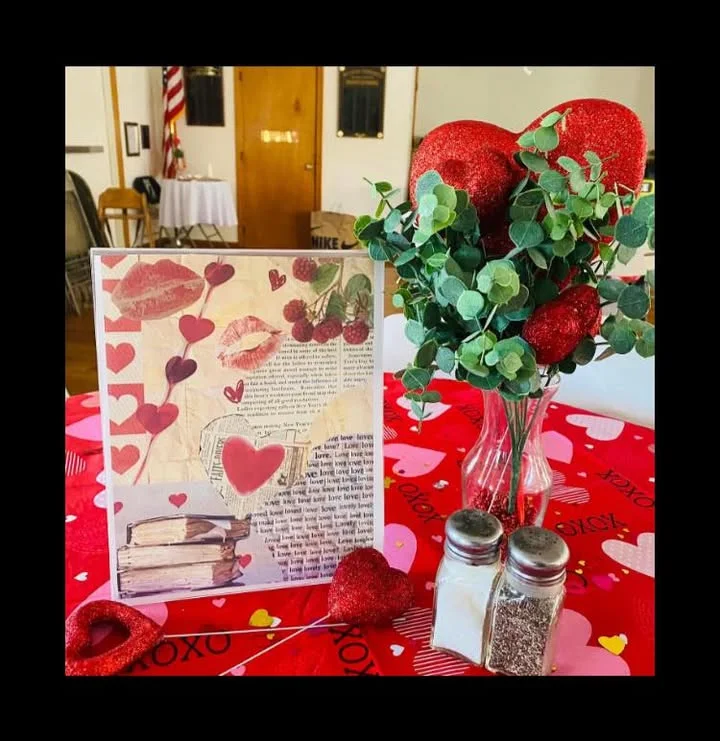 A decorative table centerpiece featuring a love-themed card, a bouquet with red hearts, and a patterned table covering.