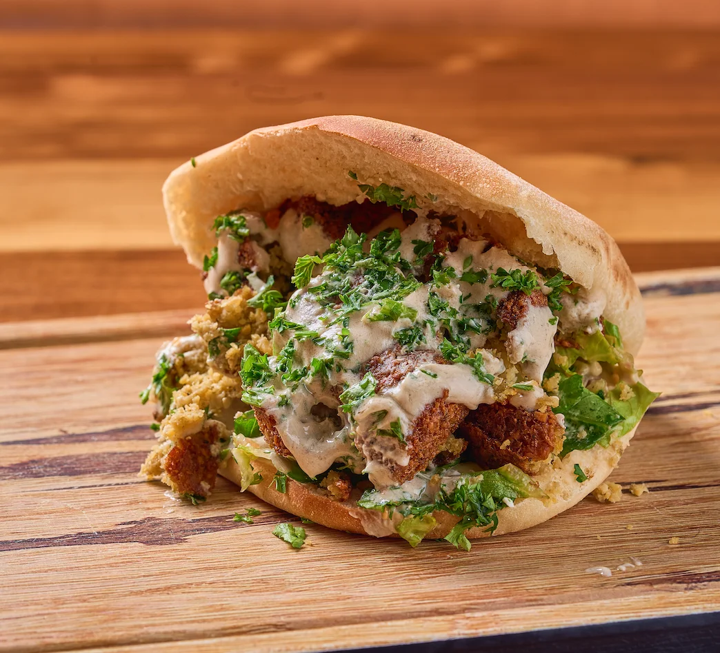 Falafel sandwich with a filling of falafel pieces, hummus lettuce, chopped tomatoes, and Tahini sauce.