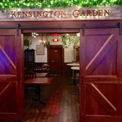 The entrance to a dining space named 'Kensington Garden' featuring wooden doors and decorative plants.