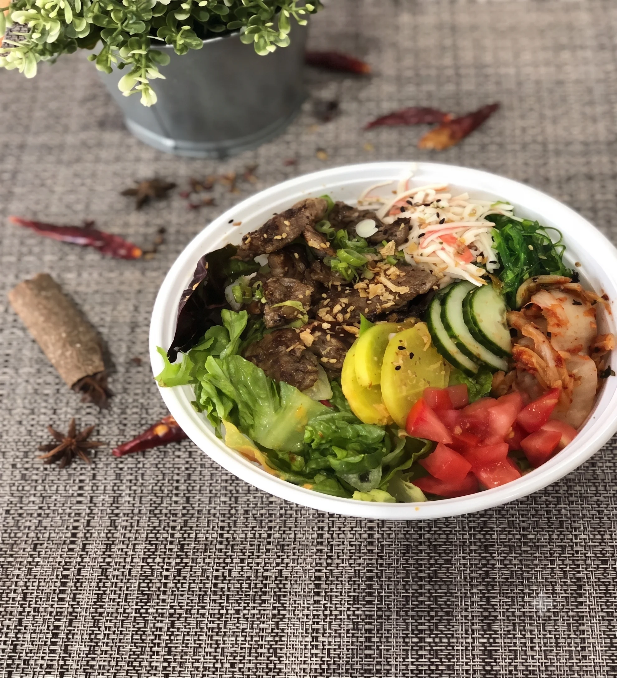 A colorful bowl of beef, vegetables, and kimchi on a textured surface.