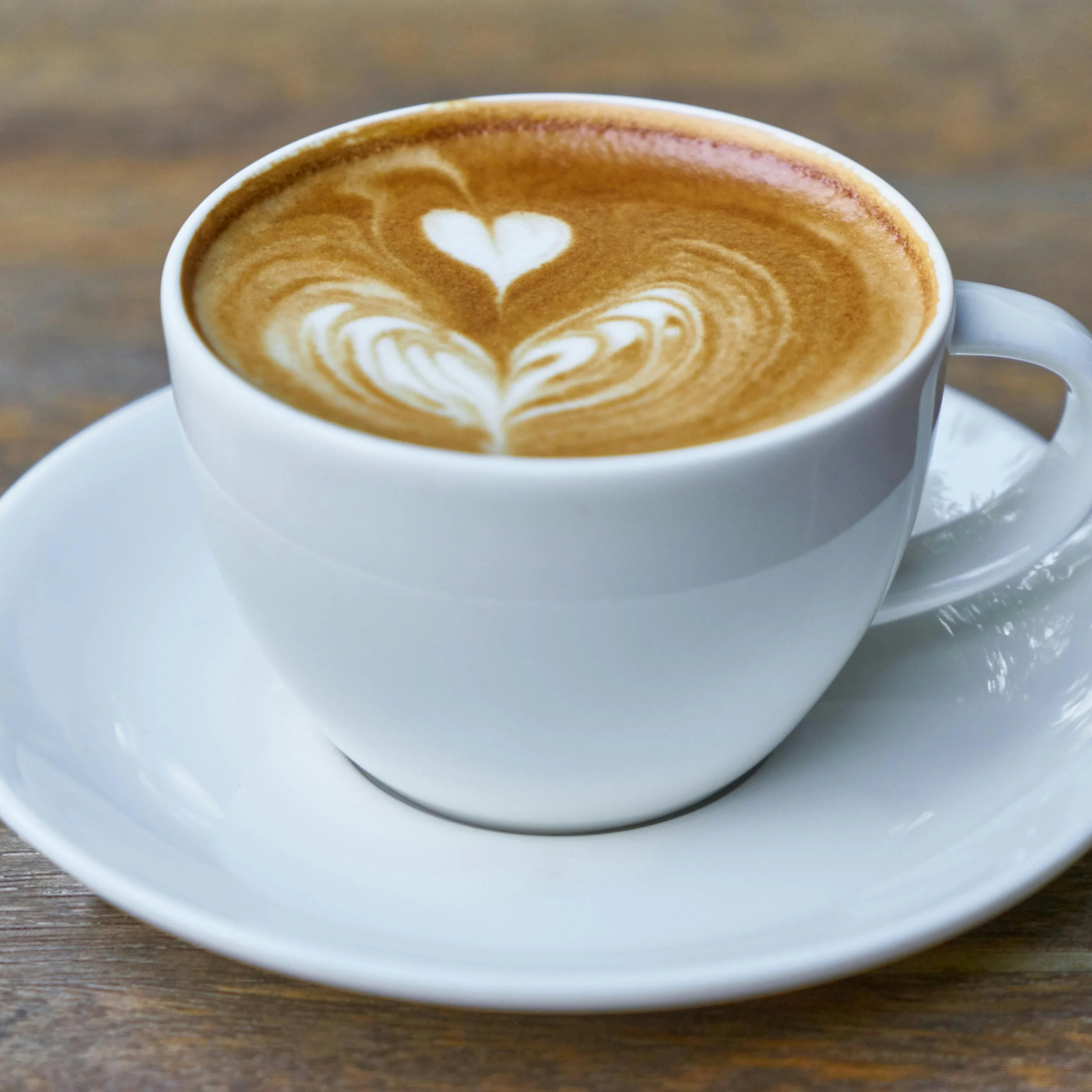 Latte art heart in a white cup on a wooden table
