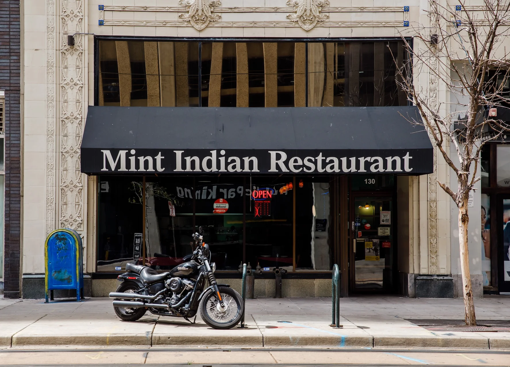 The storefront of Mint Indian Restaurant on Stout Street in Denver, showing its classic black awning below an ornate building facade.