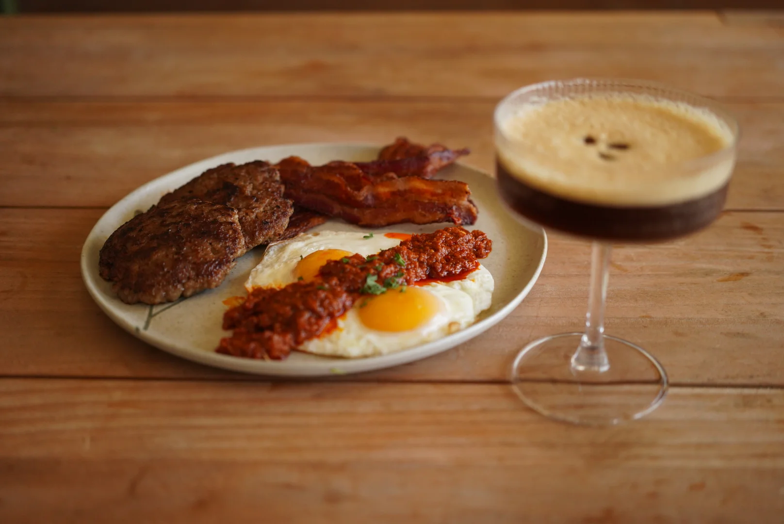 A table setting featuring a bowl of soup, a bottle of cider, a bagel with toppings, and a cocktail glass. The scene is cozy with wooden flooring and casual decor.
