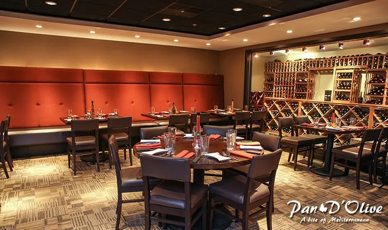 An elegant indoor dining area featuring wooden tables and chairs, with red accents on the walls and a wine display in the background.