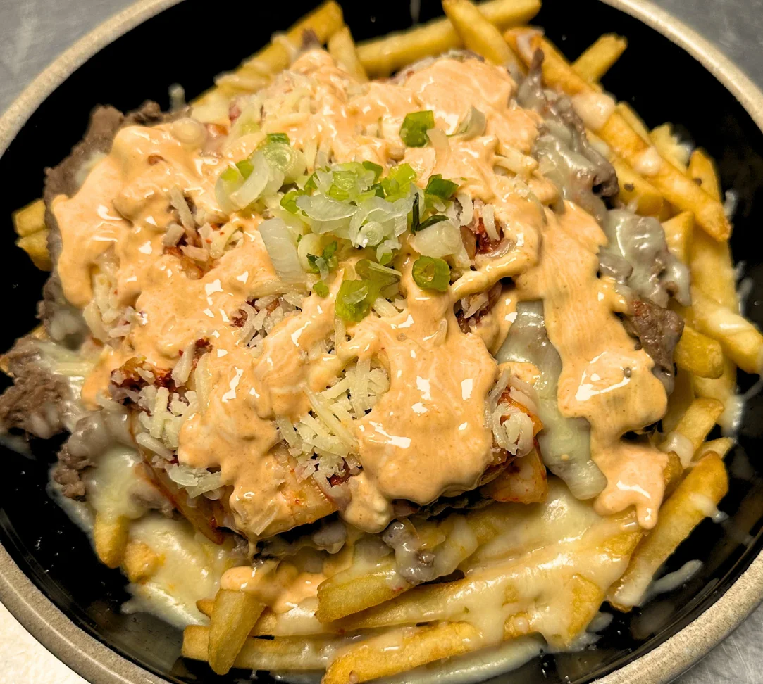 Loaded fries topped with cheese, beef, and sauce in a bowl.