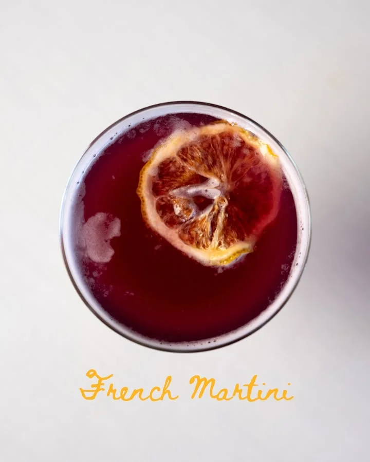 A vibrant cocktail with a slice of dried orange floating on top, presented in a clear glass.