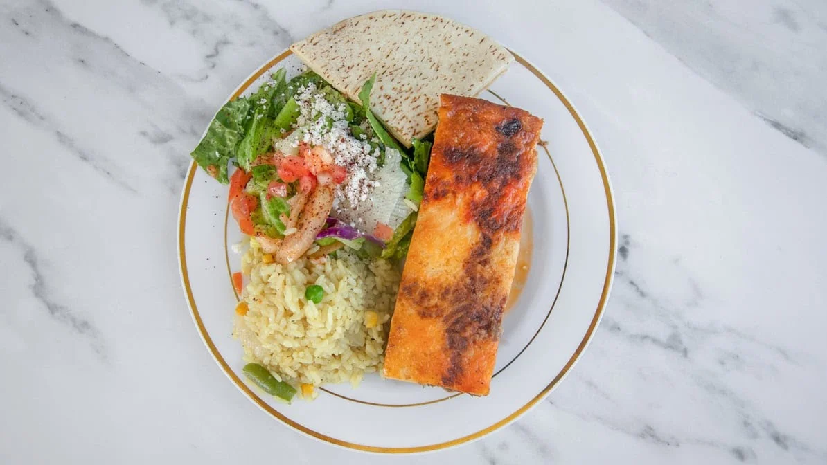 A flavorful dish with grilled fish, yellow rice, a fresh salad, and a piece of flatbread served on a decorative plate.