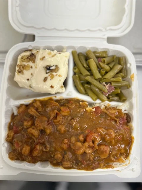A food container featuring a serving of shrimp stew with rice, green beans, and a dessert topped with nuts.