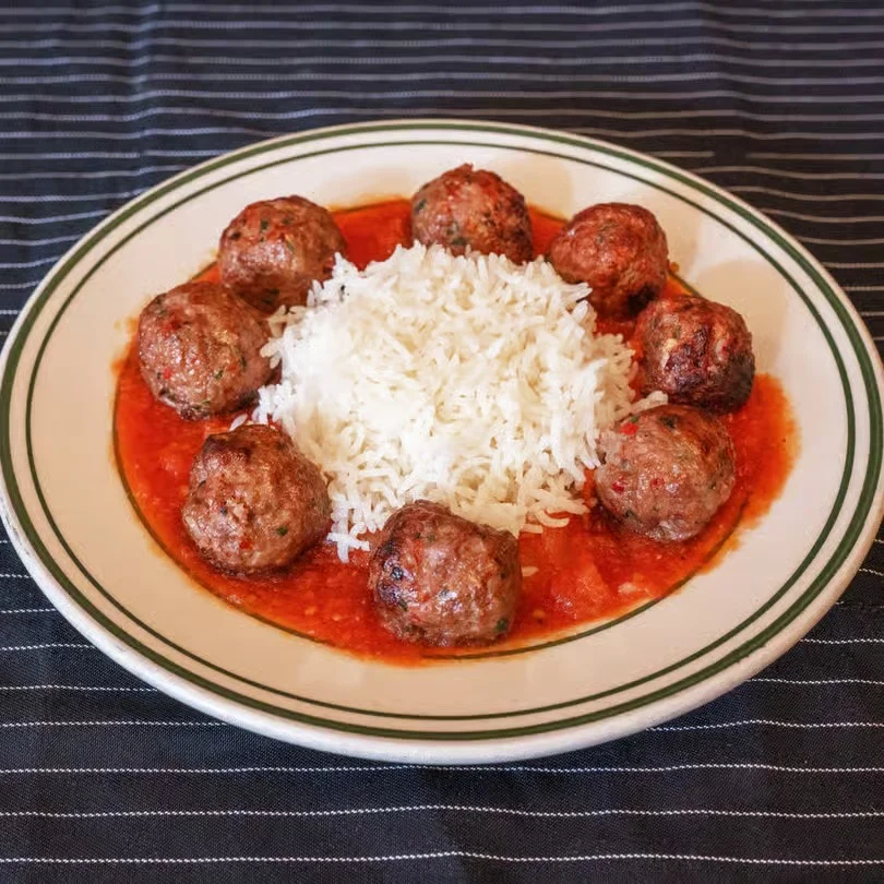 Plate of meatballs in tomato sauce served with white rice.