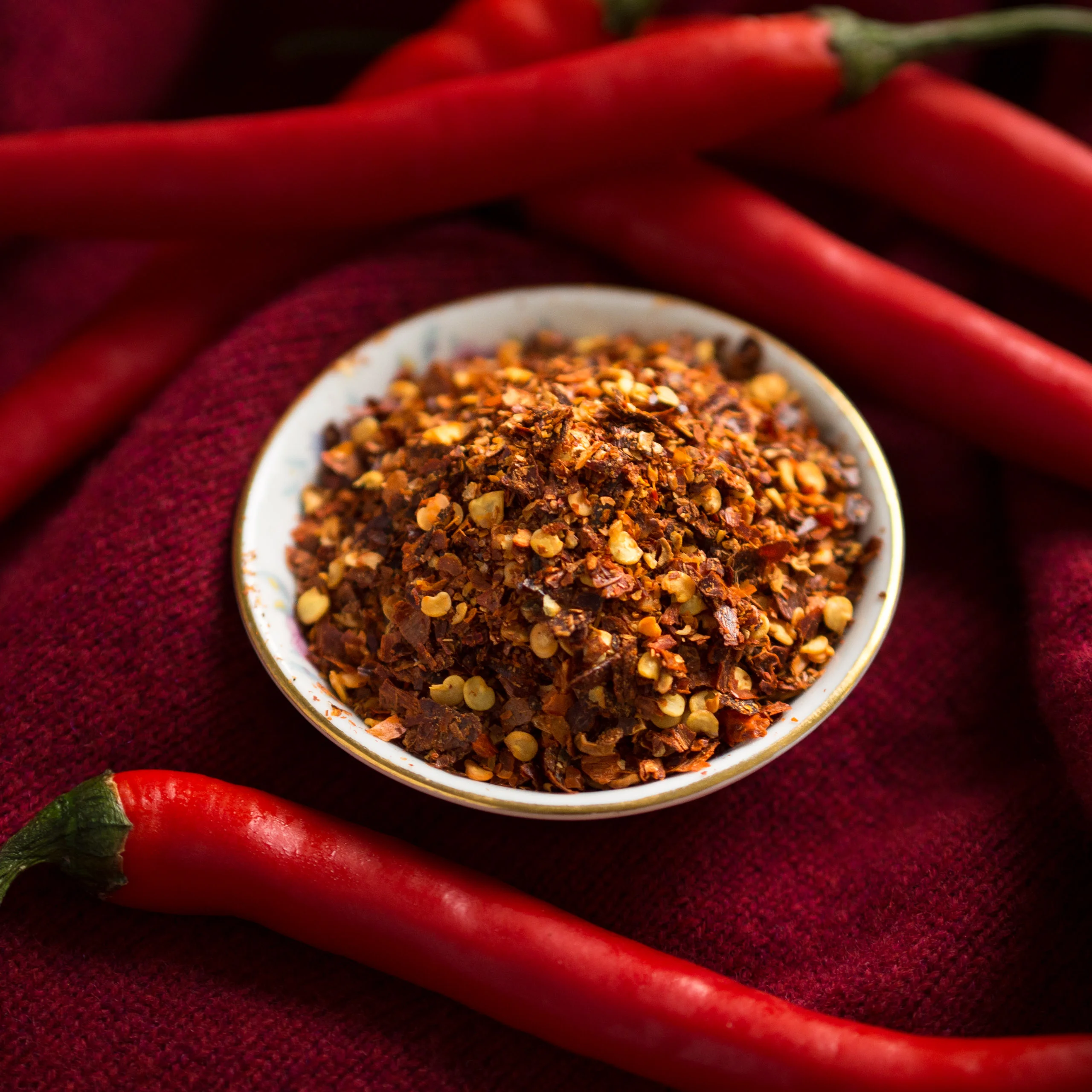 Bowl of chili flakes surrounded by fresh red chilies