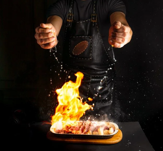 Flaming grilled meat dish being prepared in a restaurant kitchen