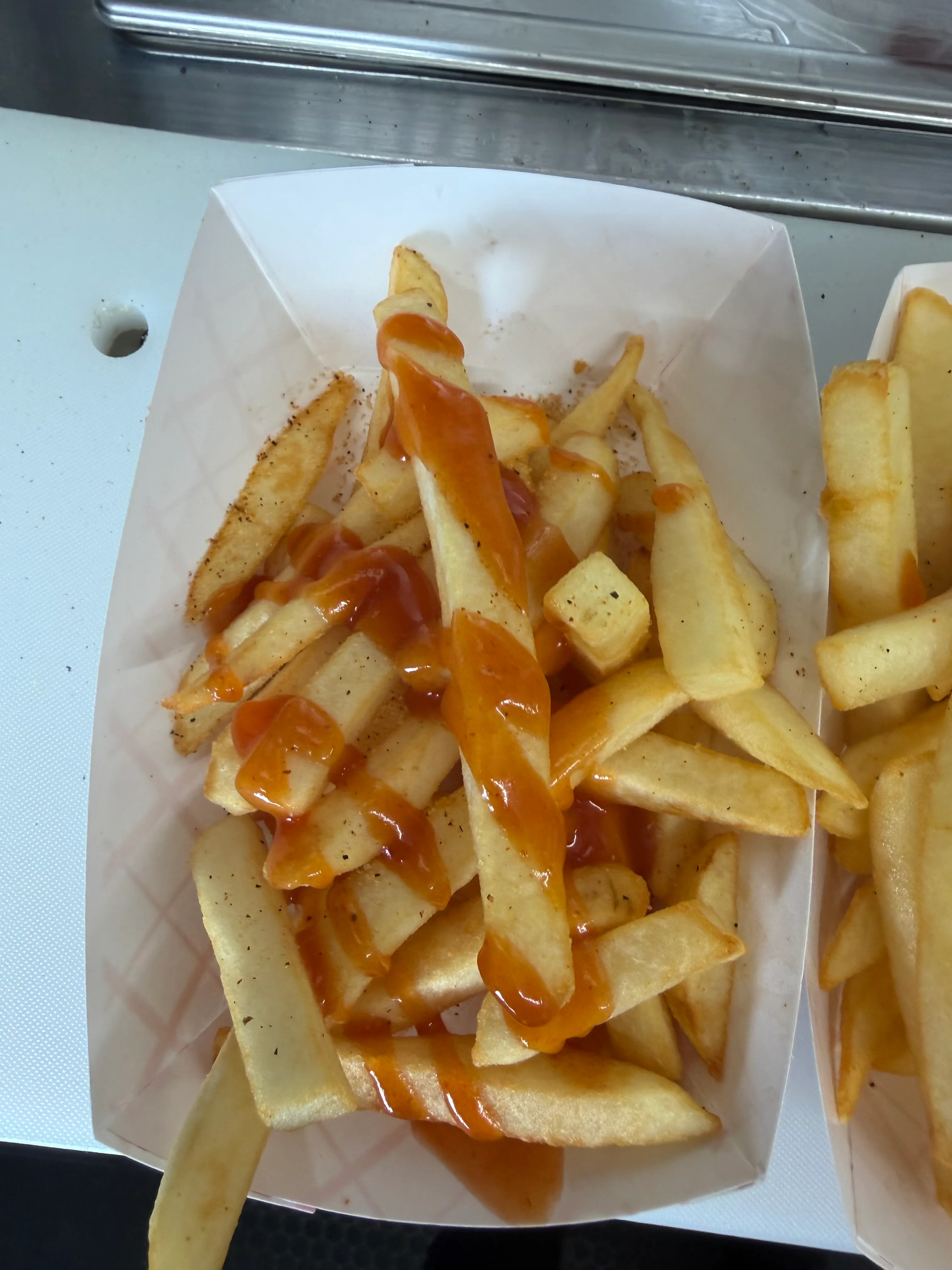 A serving of french fries drizzled with a sweet sauce, served in a paper tray.