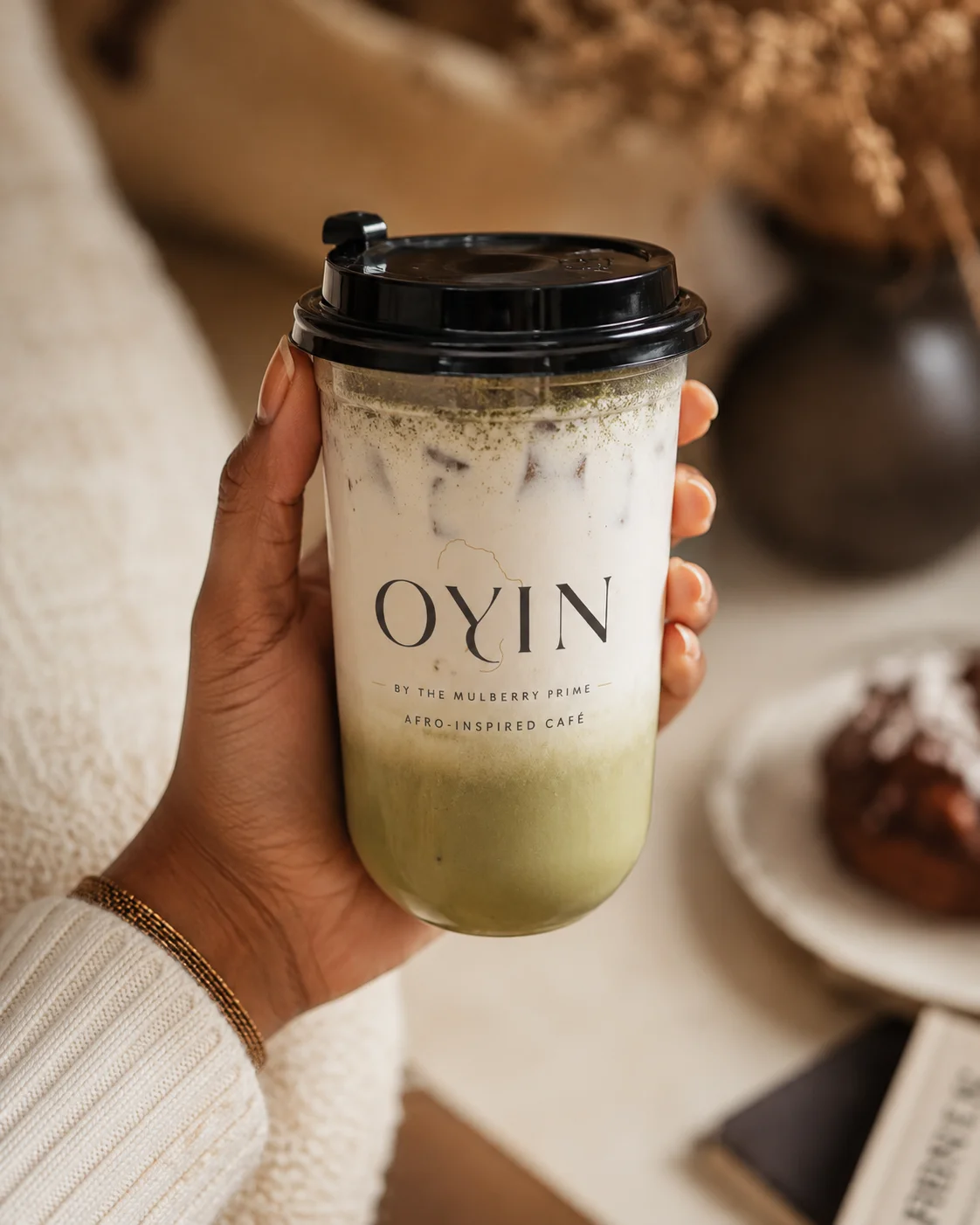 Iced matcha drink in a clear cup held by a hand, with a cozy background.