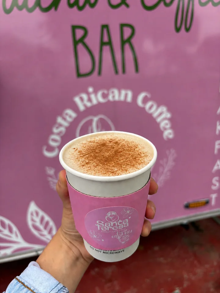 A cup of creamy beverage topped with cinnamon, displayed against a pink background featuring coffee branding.