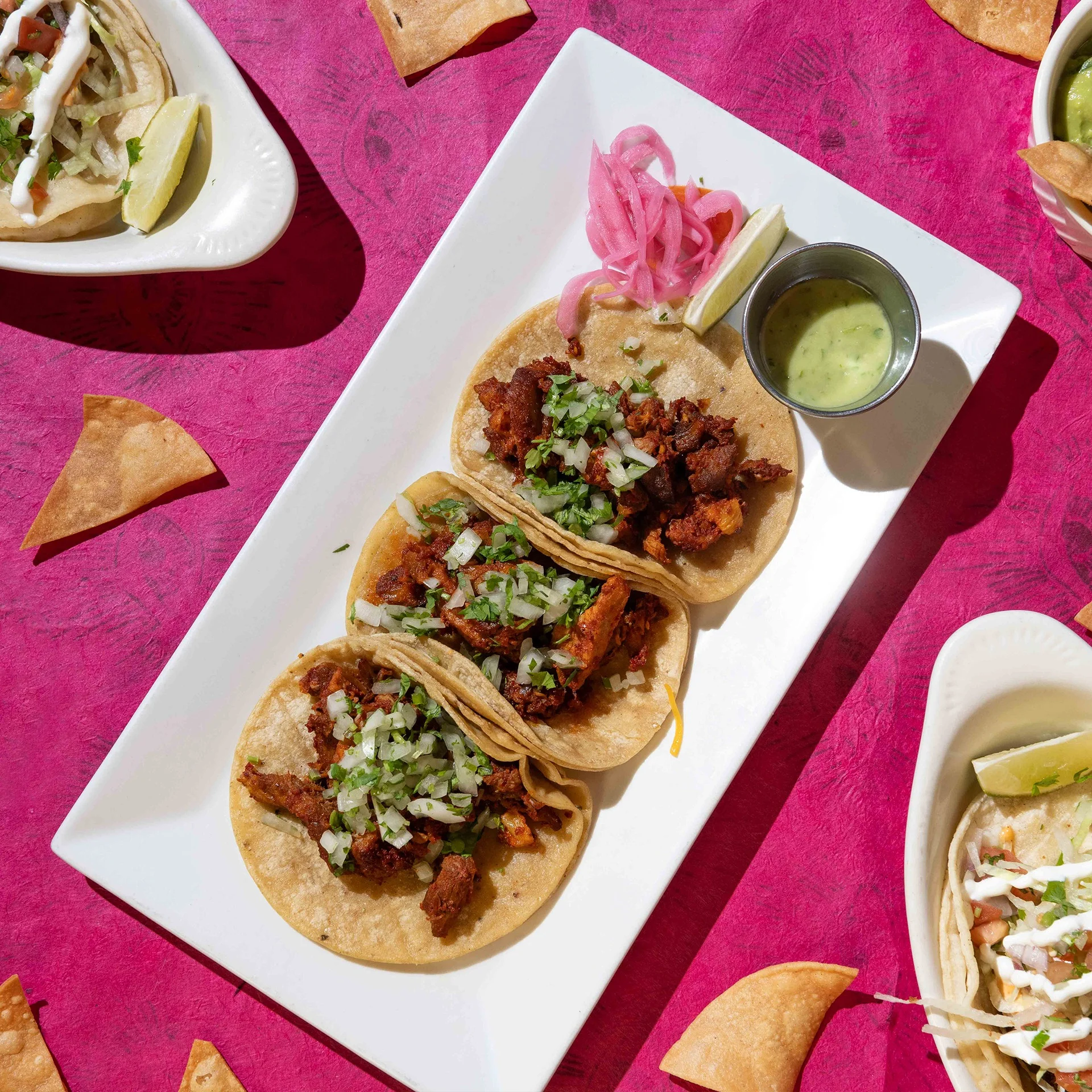 Three tacos topped with cilantro and onion, served with salsa and pickled onions at Friducha in Brooklyn, NY.