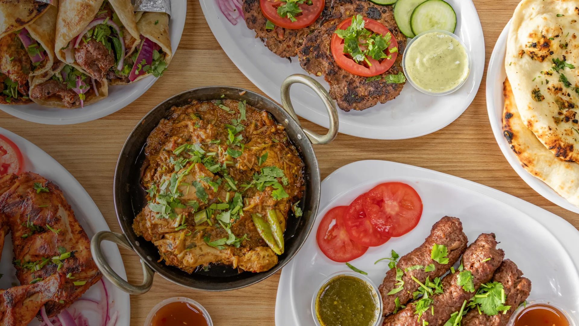 Assorted Pakistani BBQ dishes including chicken karahi, seekh kebabs, paratha rolls, naan, and grilled chicken served with chutneys and salad at Karachi BBQ Tonight.
