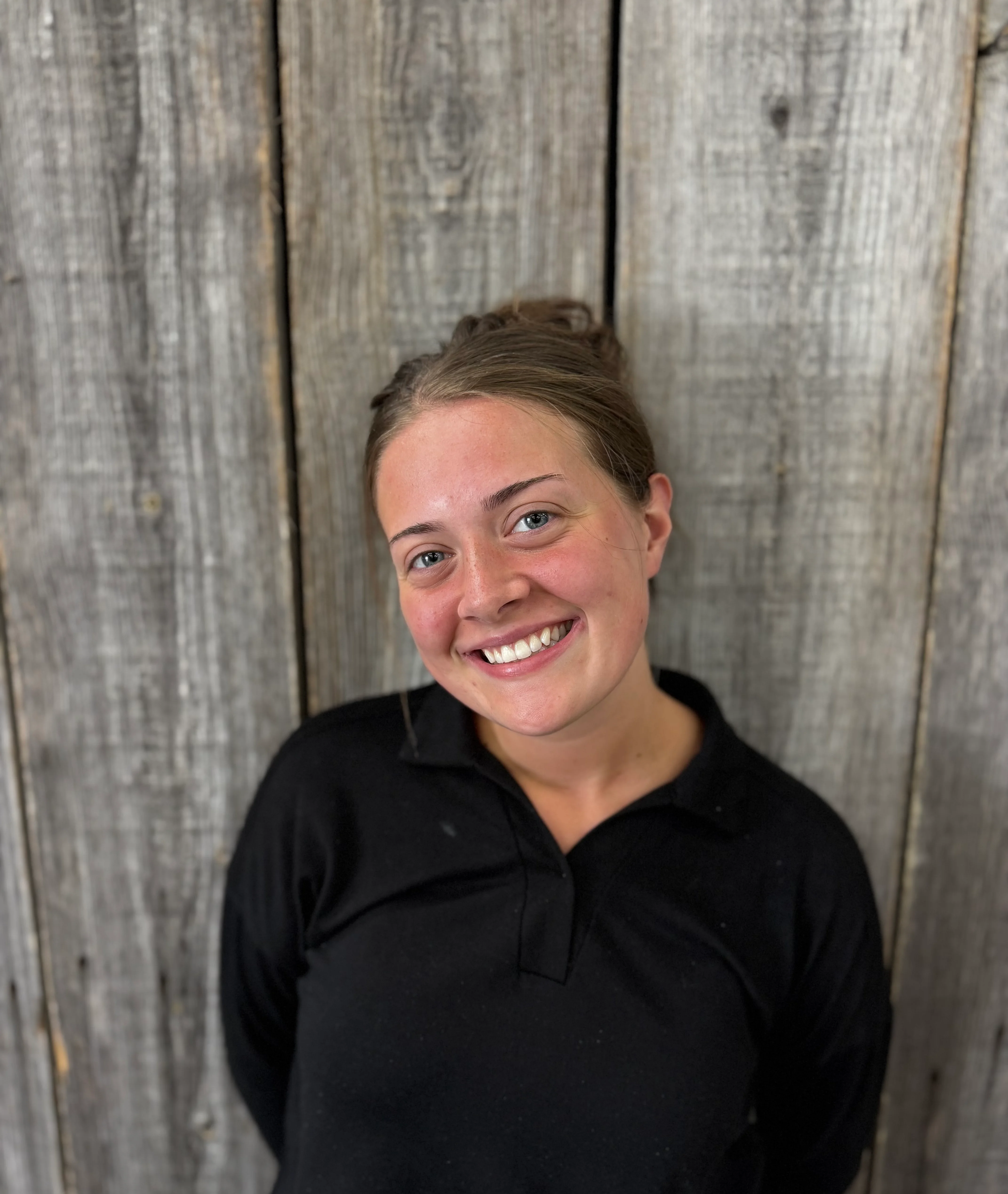 Smiling young woman in a black shirt against a rustic wooden backdrop