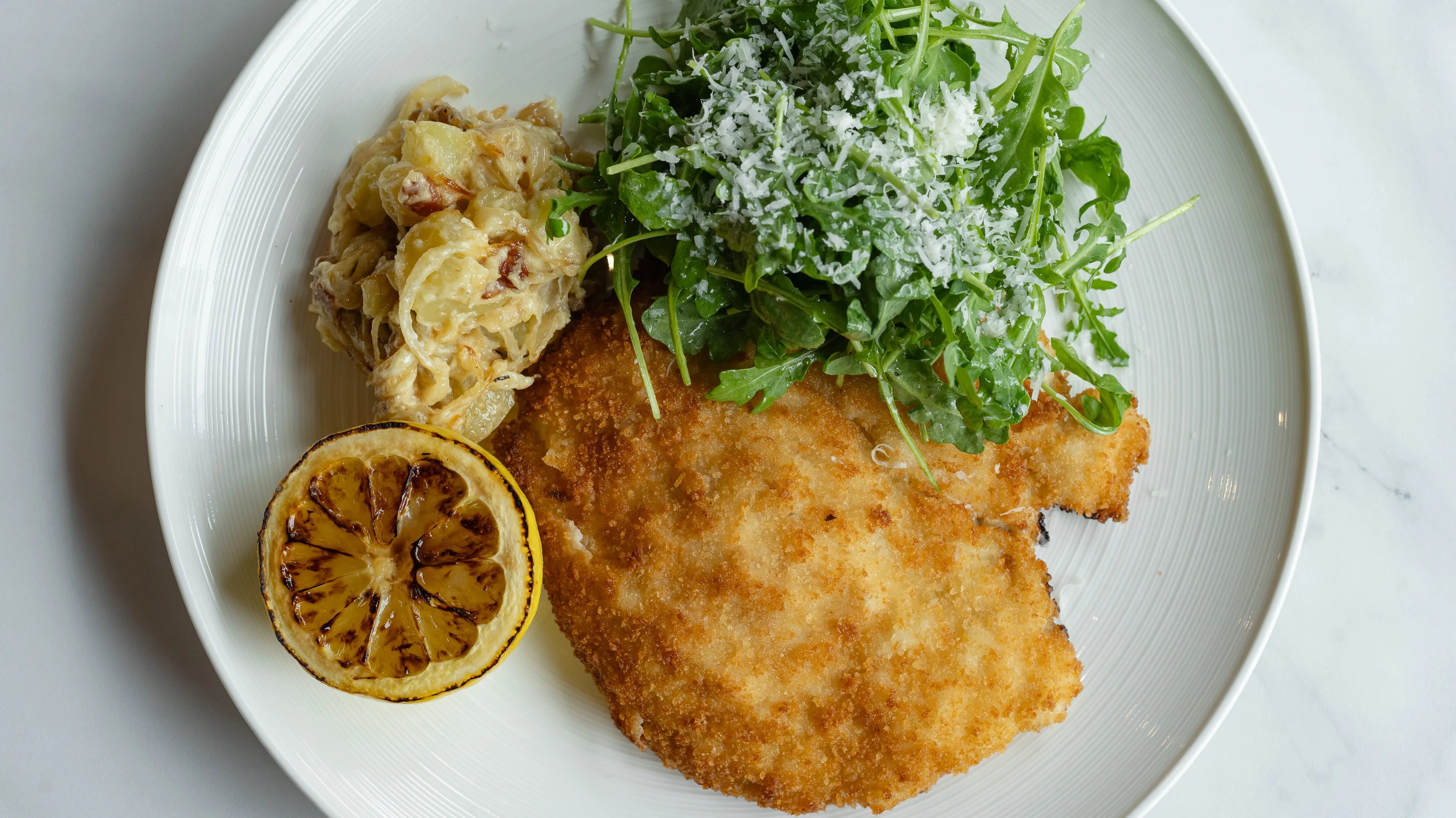 Crispy Italian cotoletta with arugula salad and roasted lemon