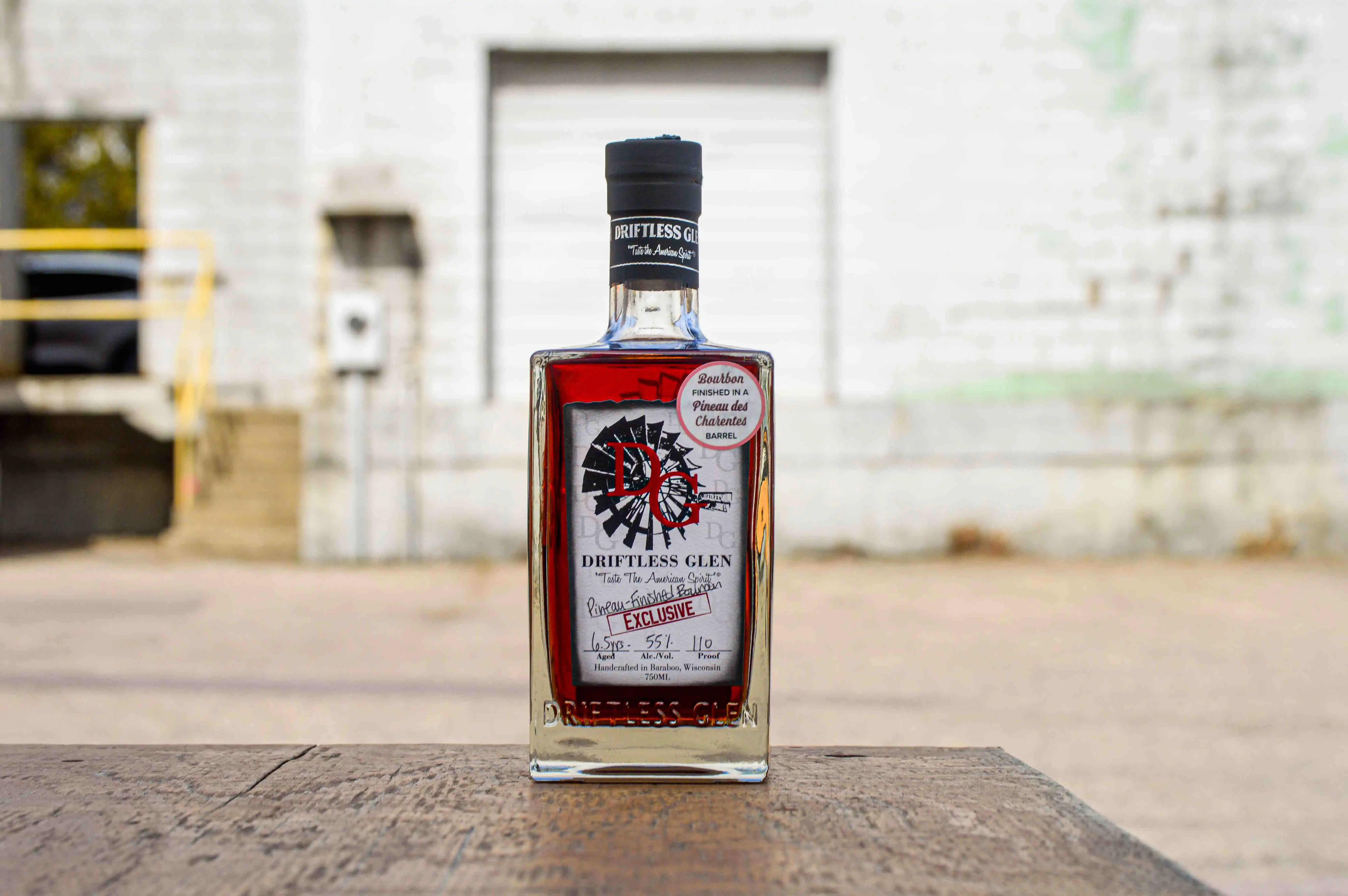 A bottle of Pineau-Finished Bourbon sits outside with a bright white background made of stone.