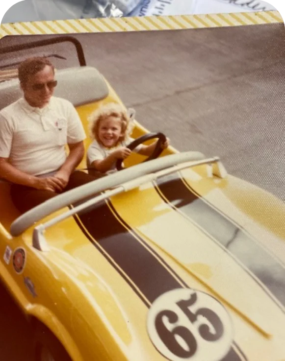Child smiling in a yellow go-kart with an adult driver