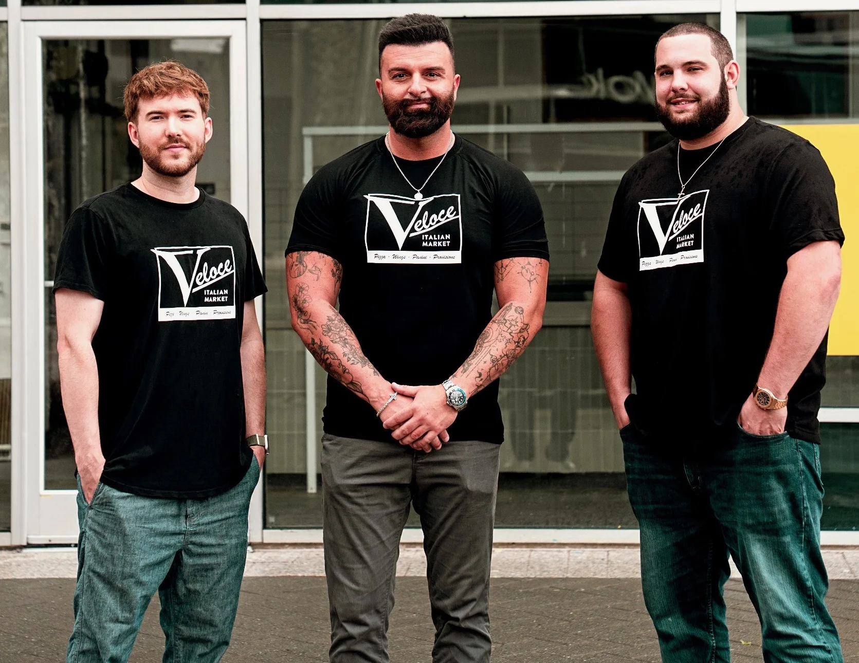 Three restaurant staff members in branded shirts posing outside a modern eatery
