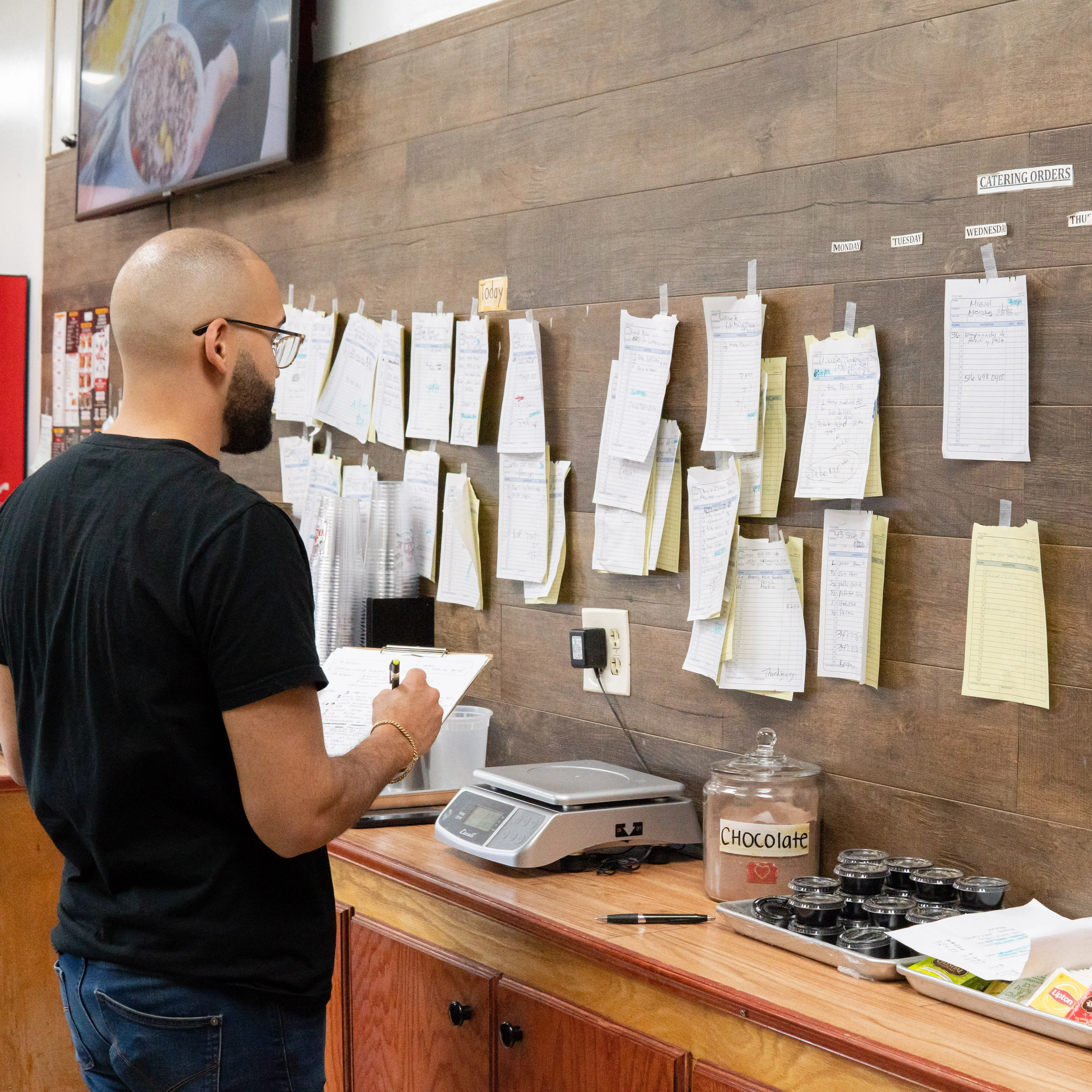 Restaurant staff reviewing catering orders on a busy kitchen wall