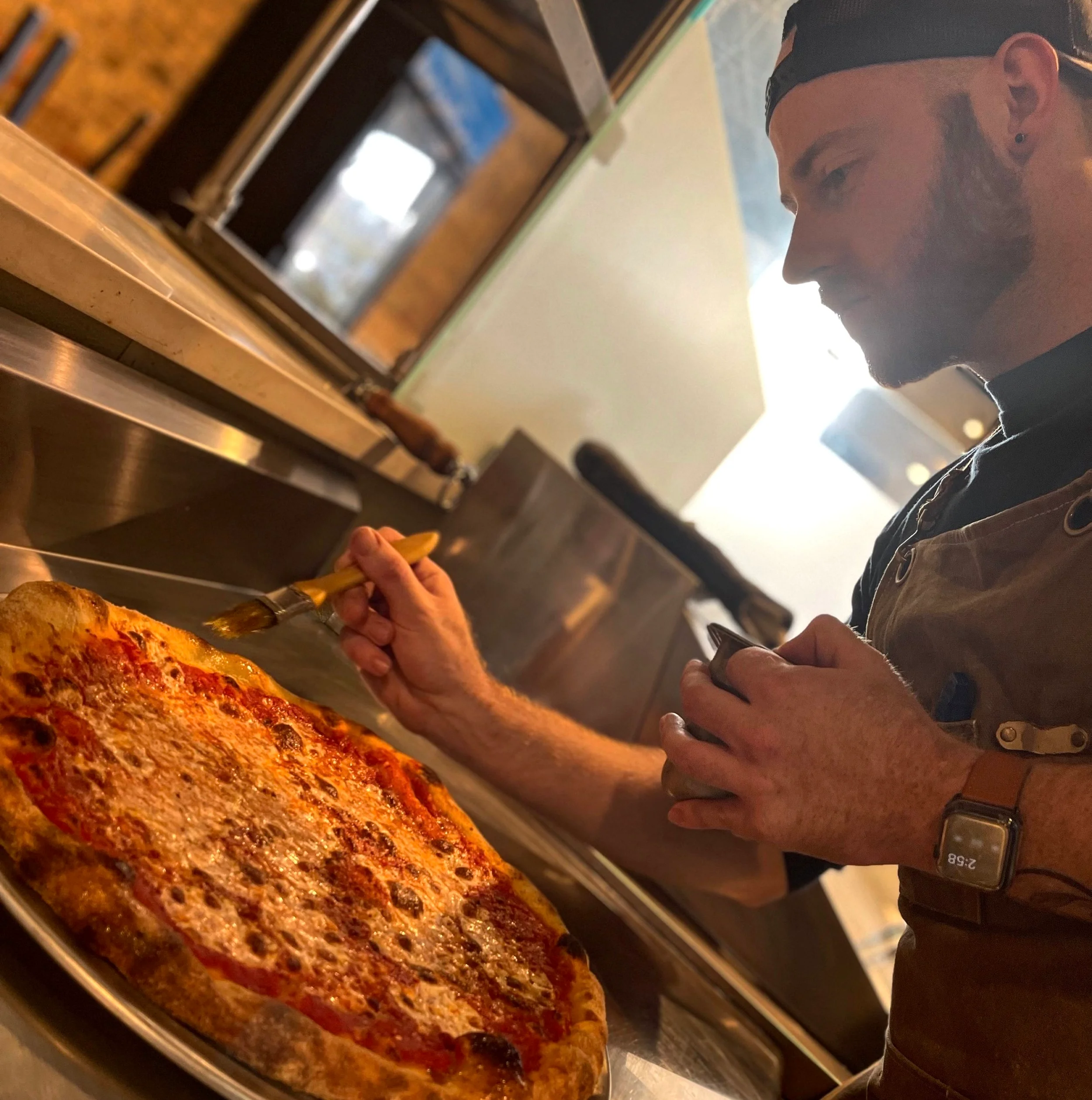 Chef brushing a Margherita pizza in a restaurant kitchen