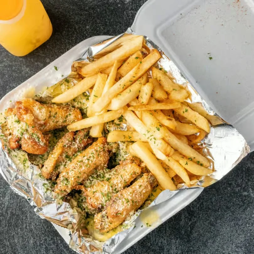 Delicious chicken wings and fries in a takeout container.