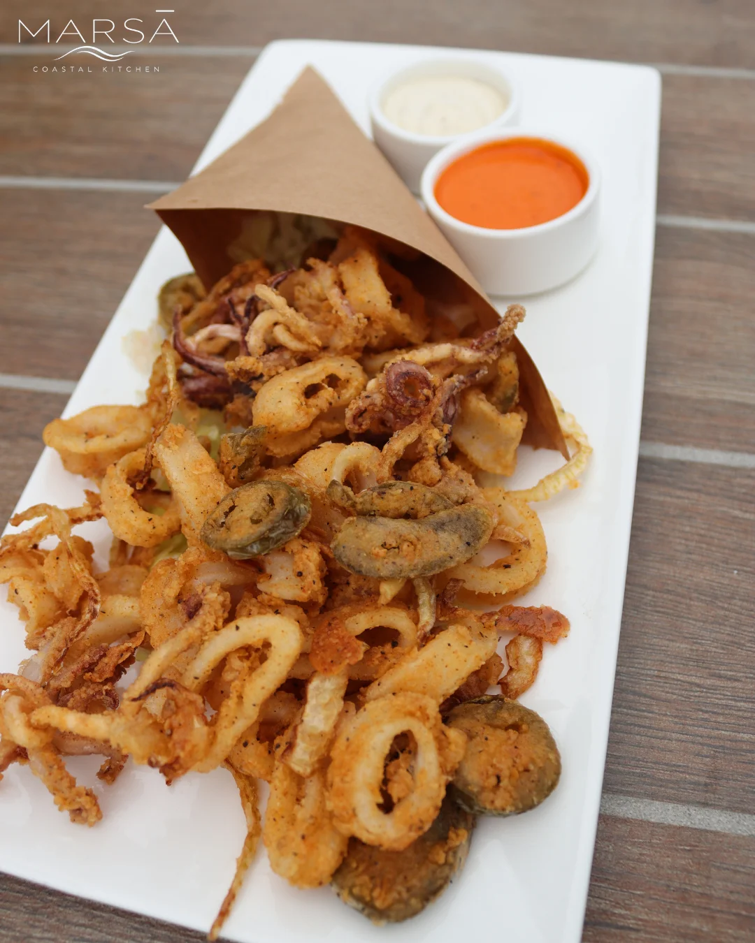 A serving of crispy calamari, accompanied by dipping sauces, presented on a white platter.