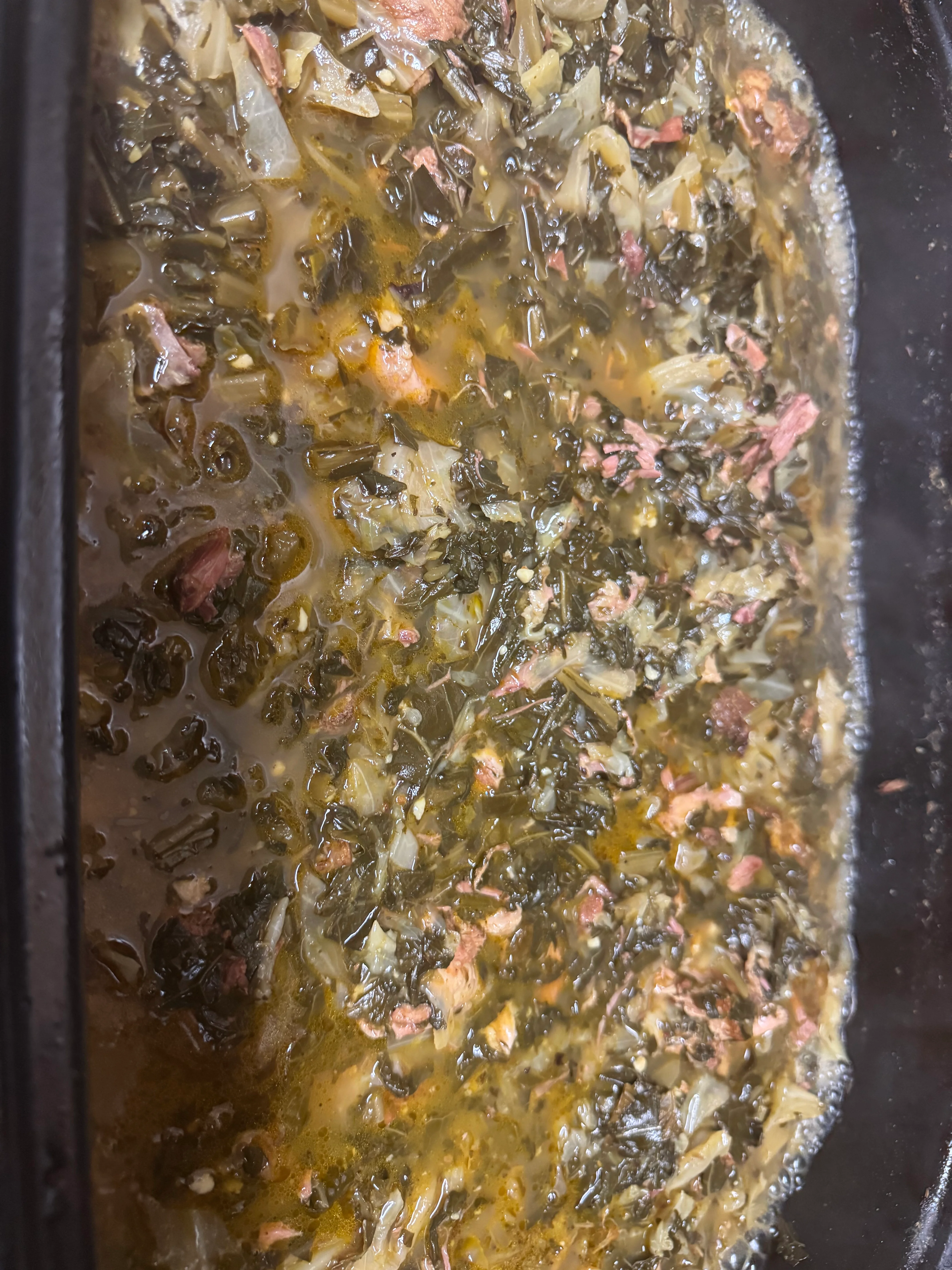 A close-up view of a simmering pot filled with greens and meat, creating a flavorful broth.