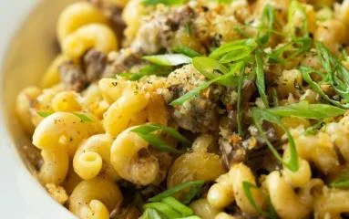 A close-up of macaroni pasta with beef and sprinkled with green onions for garnish.