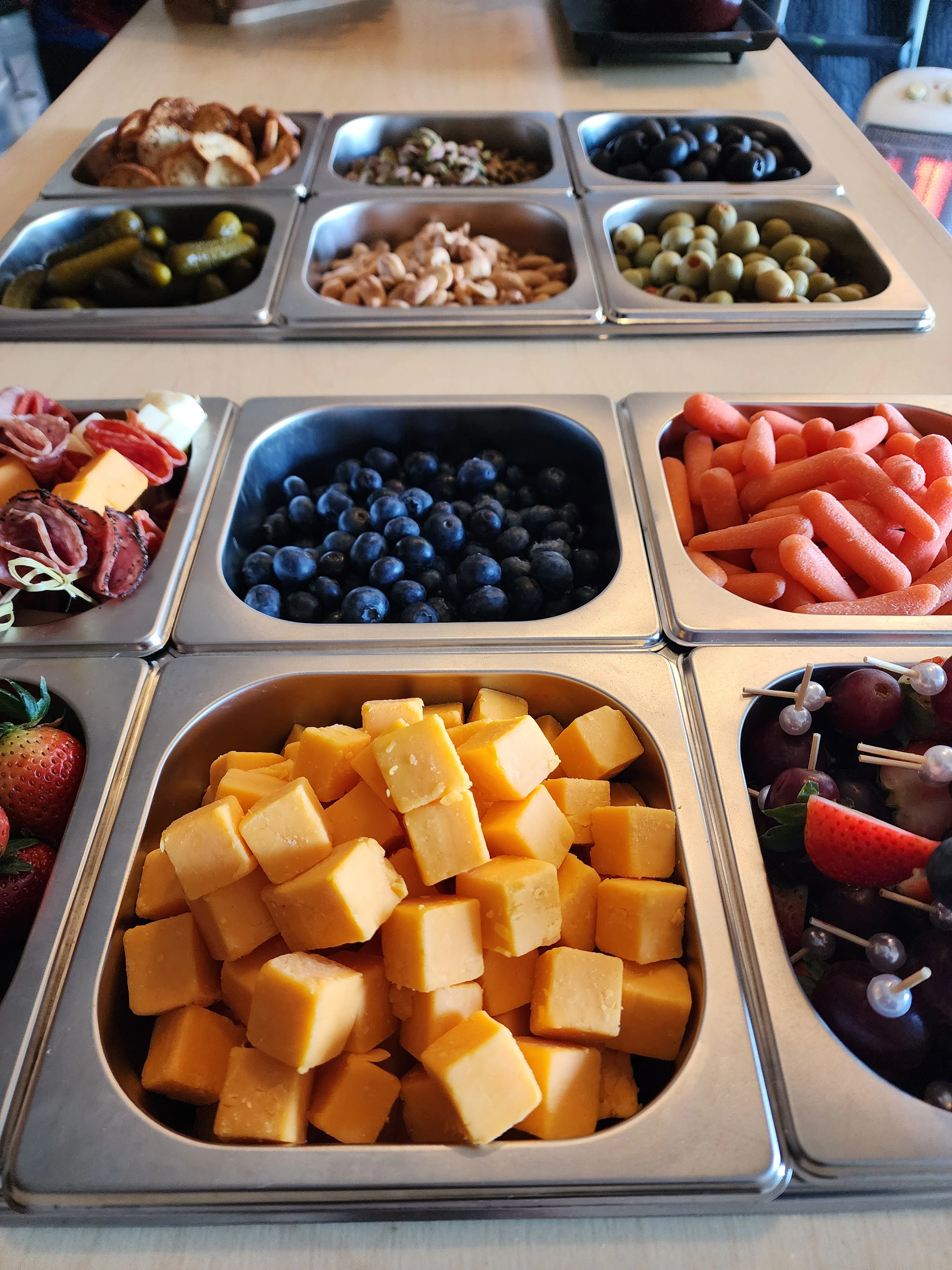 A variety of snacks displayed in metal trays, including cheese cubes, fruits, and vegetables.