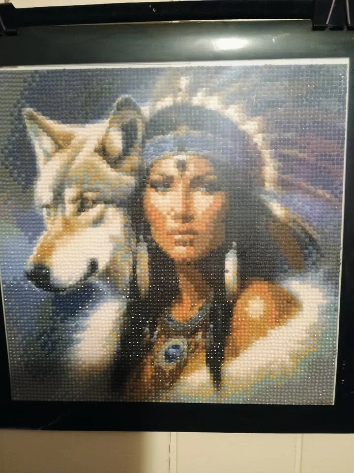 A diamond painting featuring a woman with long hair adorned with feathers and a large wolf by her side, set against a colorful background.