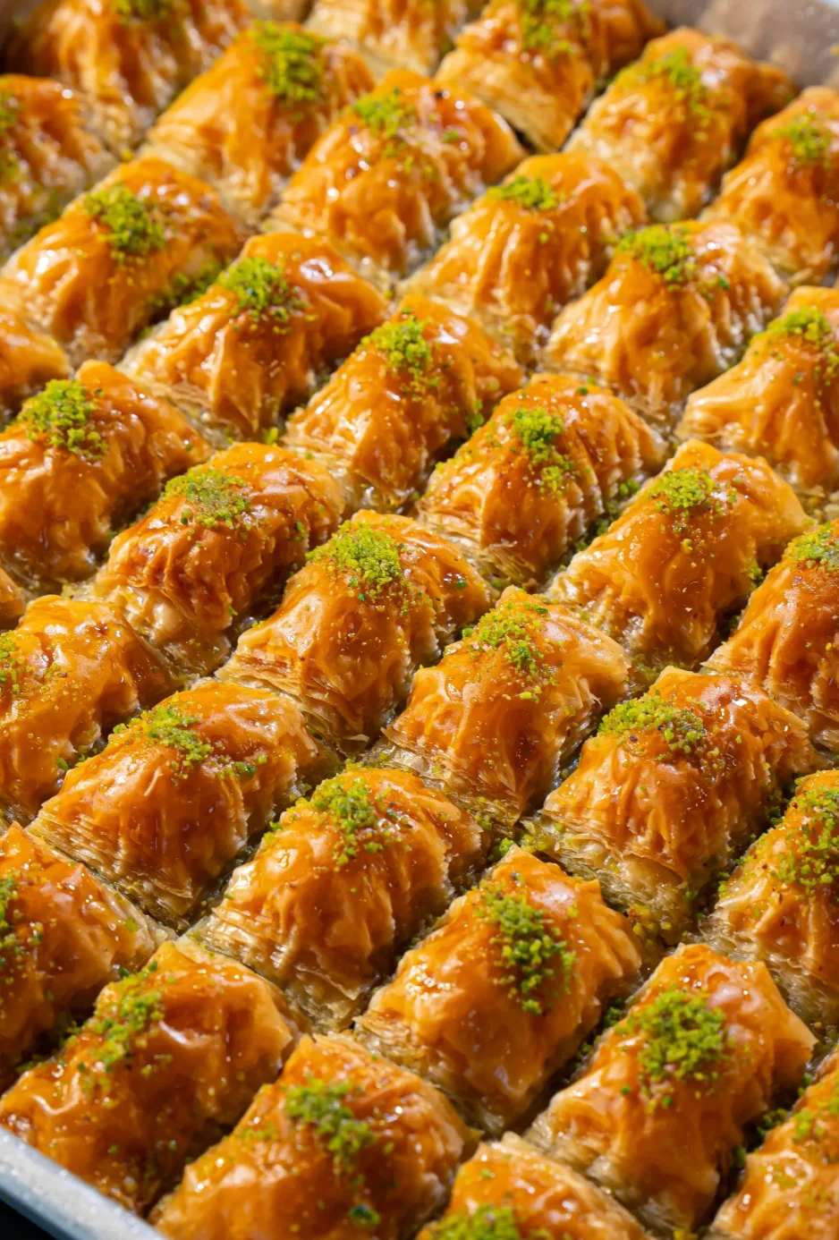 A close-up view of multiple pieces of baklava arranged neatly, showcasing a crispy, golden-brown pastry topped with finely chopped pistachios.