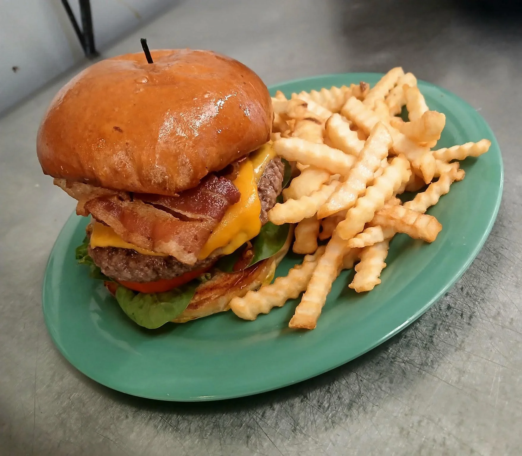 Juicy cheeseburger with bacon and fries on a green plate