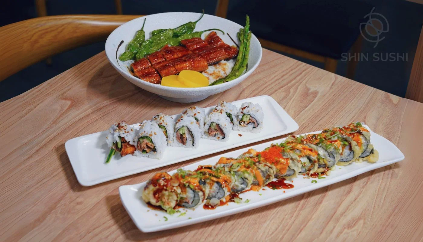 A stylized logo featuring circular shapes and an orange element, accompanied by the text 'SHIN SUSHI'.