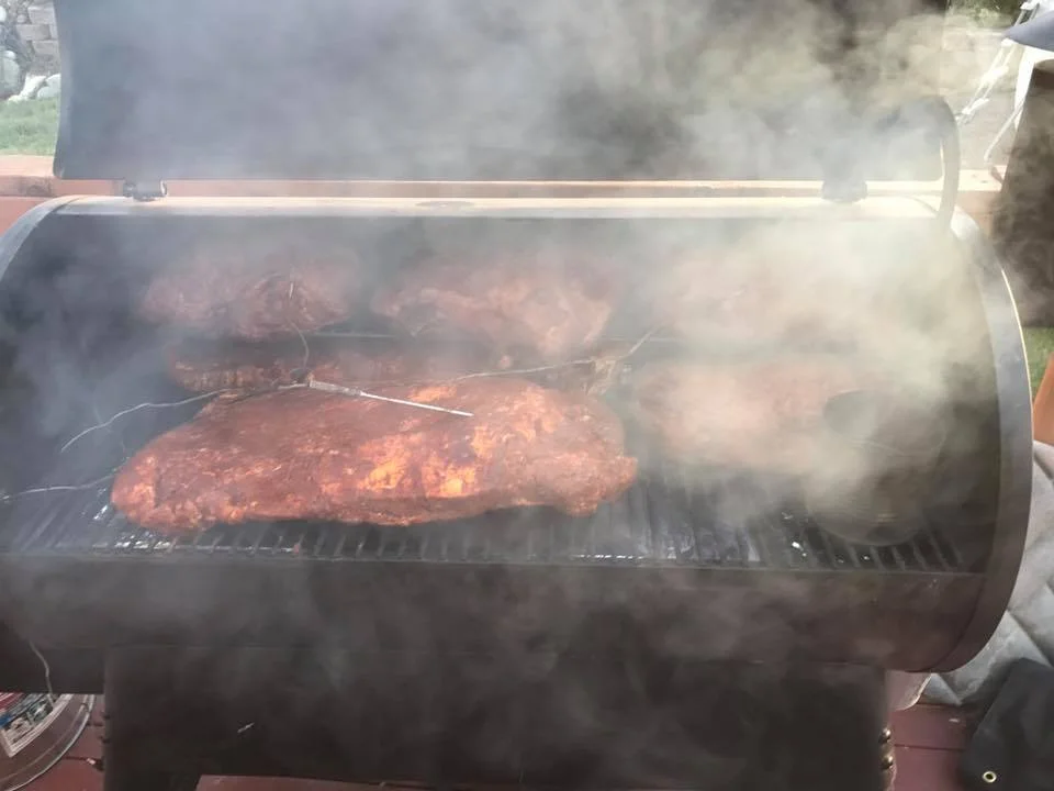 Smoky barbecue meats cooking on a grill with smoke rising.