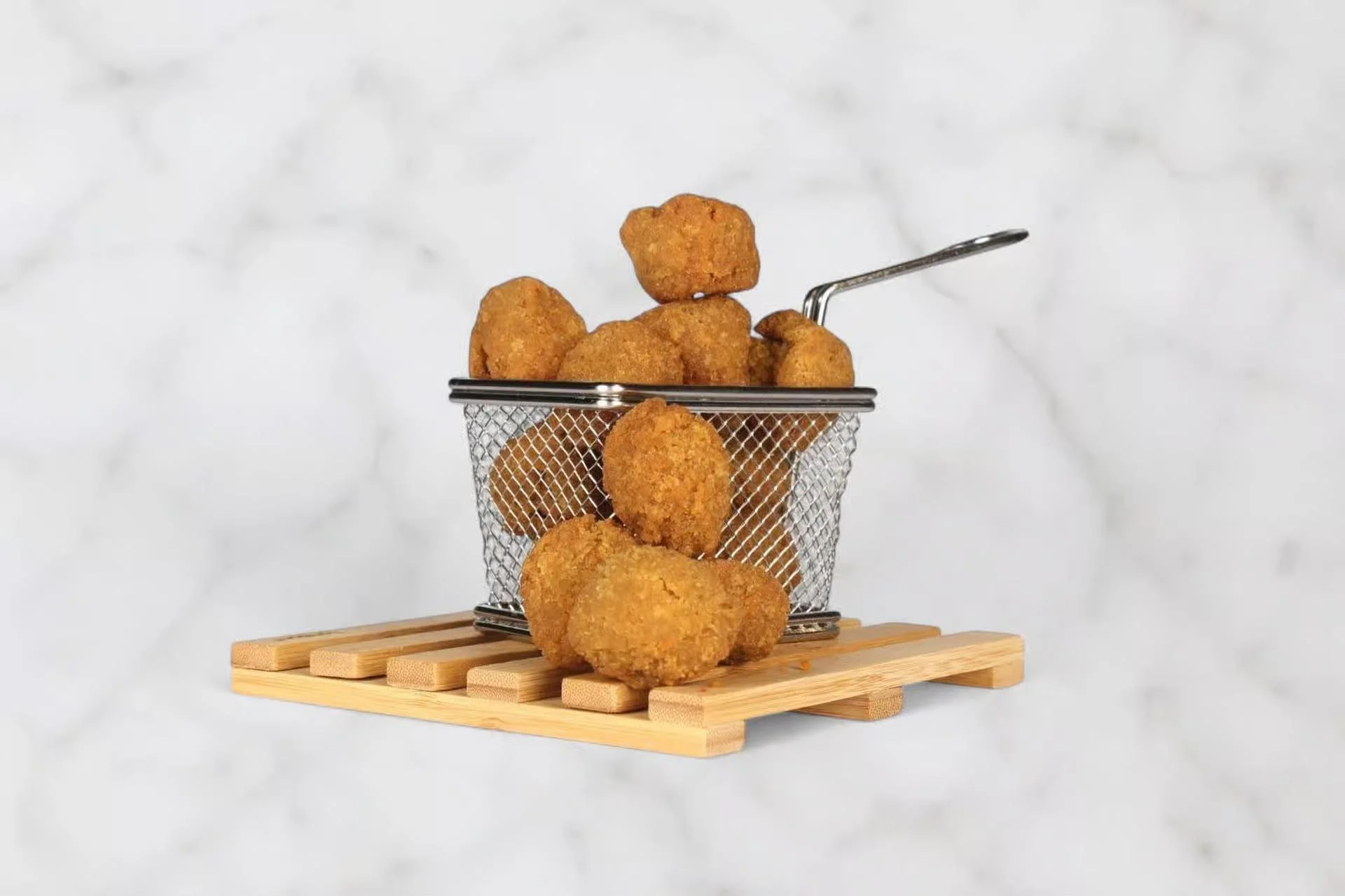 A small metal basket filled with golden-brown fried snacks, resting on a wooden base.