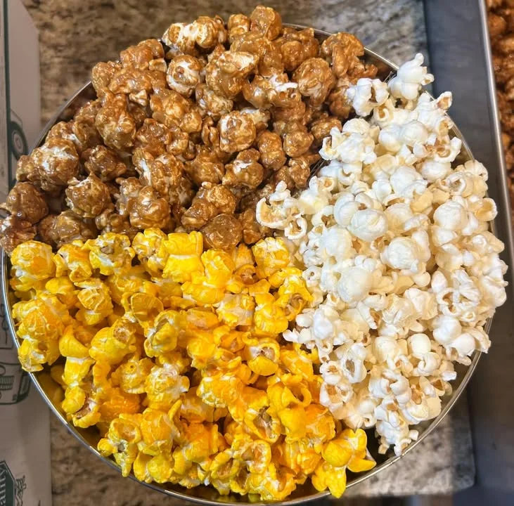 A tin filled with distinct types of popcorn, organized into sections of caramel, cheese, and buttered flavors.