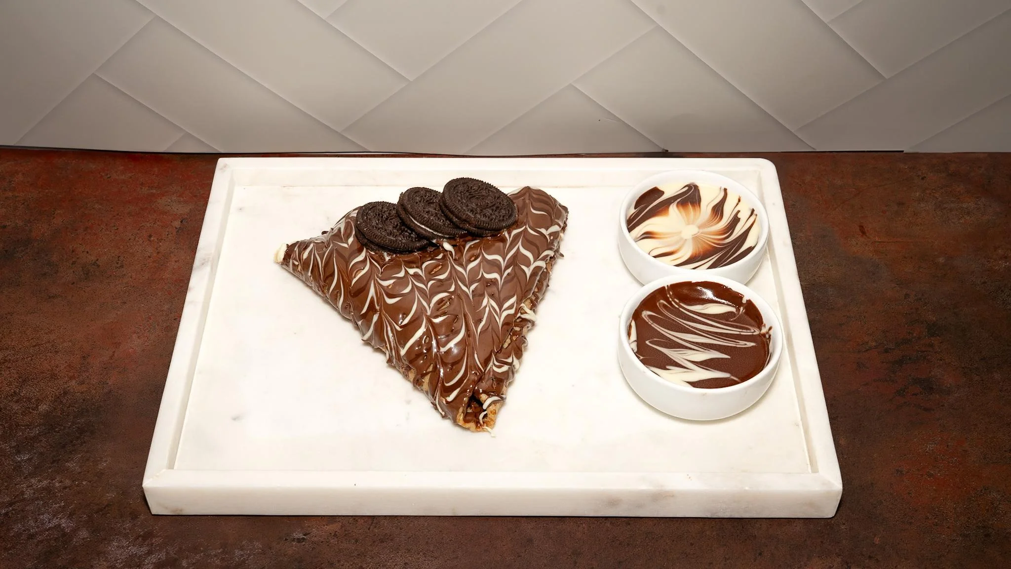 A chocolate covered crepe decorated with Oreo cookies and drizzled with chocolate sauce, served with additional dipping sauces.